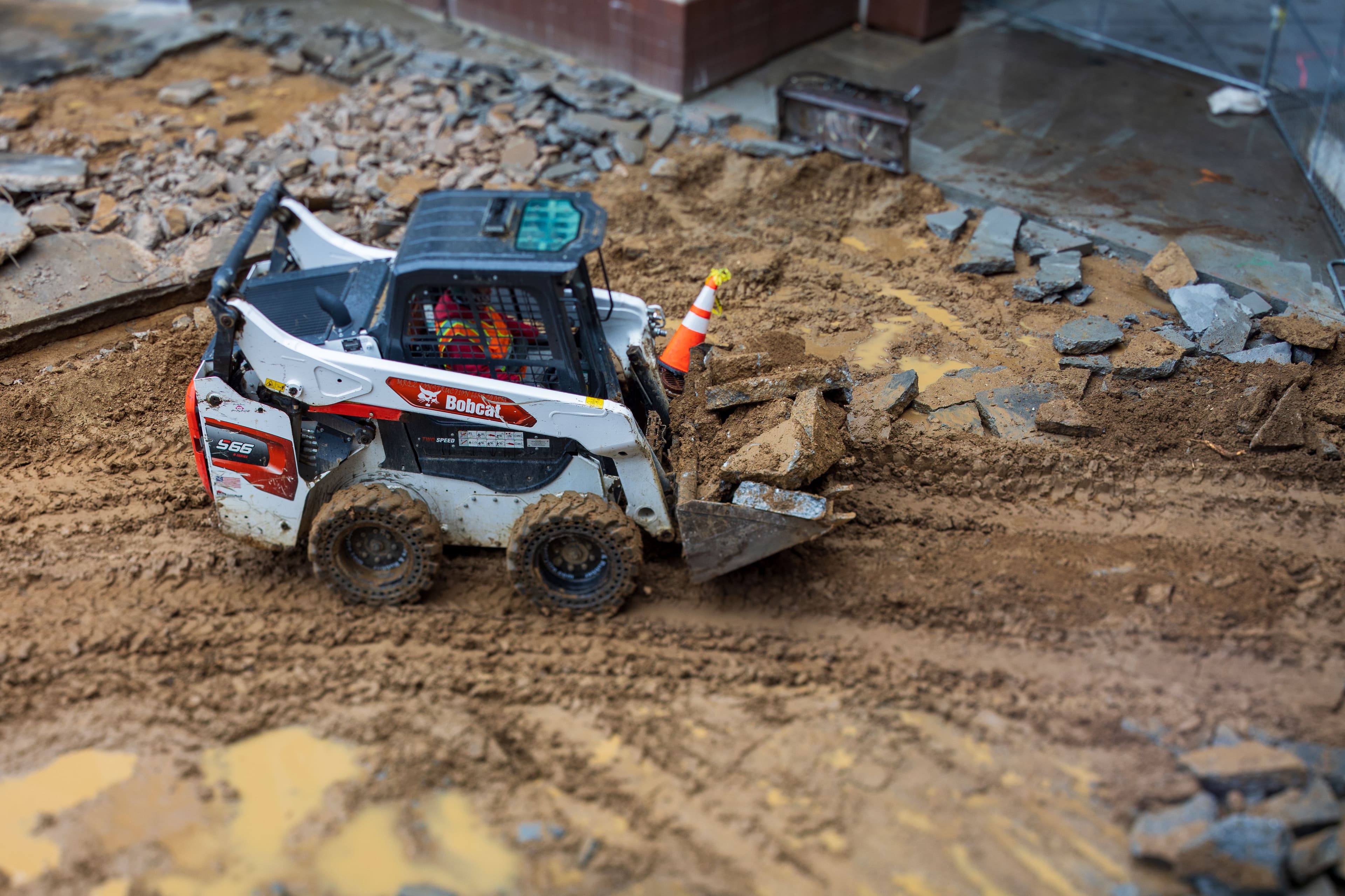White Bobcat skid-steer loader clearing mud and broken concrete debris at an active construction site.